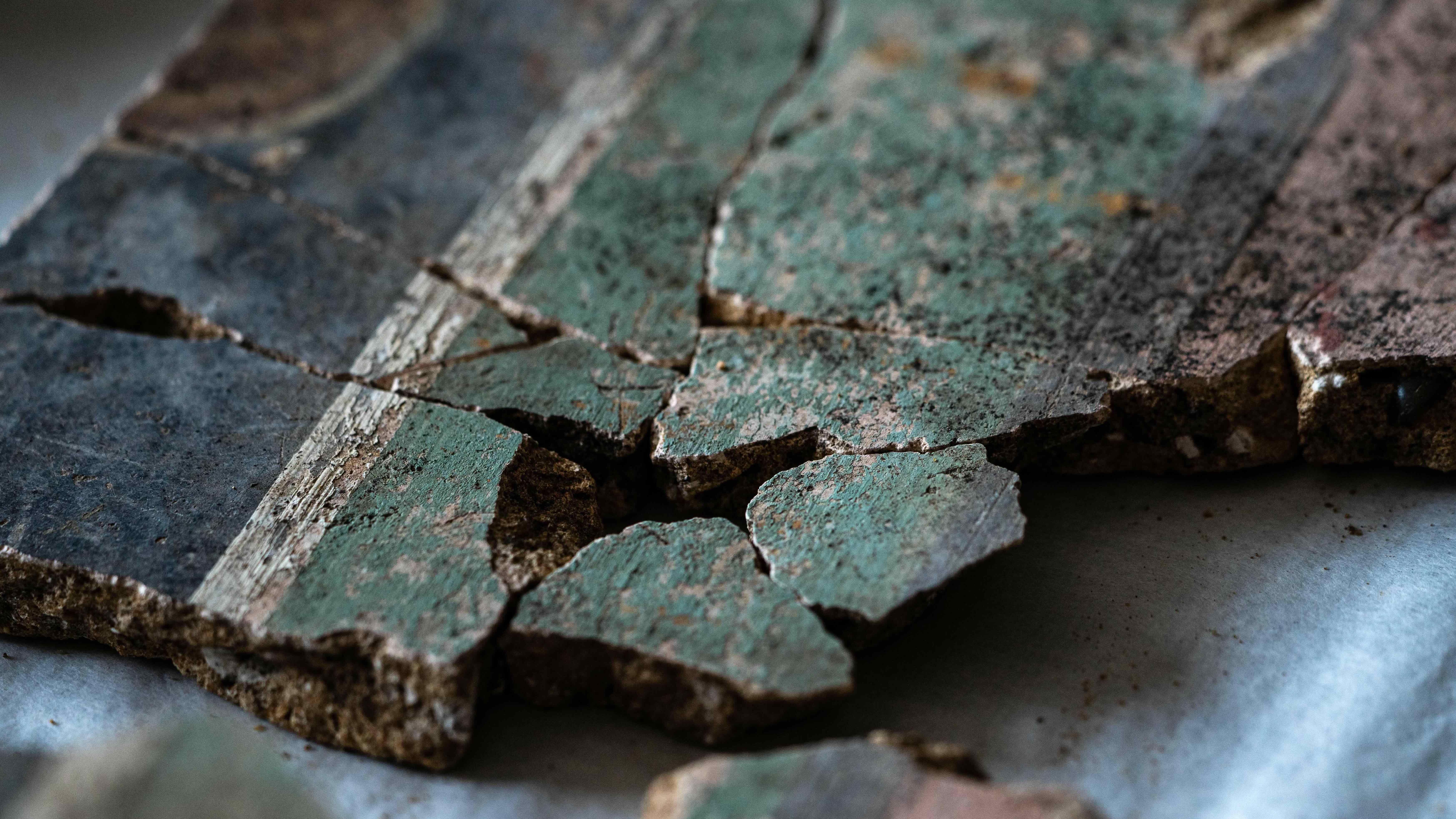 Una imagen de cerca de al menos 10 fragmentos de yeso que han sido unidos. En el lado derecho de la imagen se encuentra la sección rosa, luego una delgada línea divisoria negra y una banda verde pálido más gruesa. Hacia la izquierda de la imagen hay una fina línea divisoria blanca y luego una gruesa banda negra.