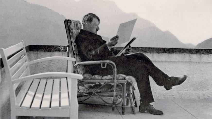Foto yang diambil sekitar 1936 ini menampilkan Adolf Hitler sedang duduk di kursi rotan di teras Berghof dengan pakaian sipil. Ia terlihat sedang membaca berkas-berkas.