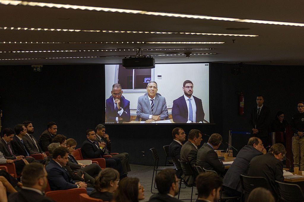 Braga Netto aparece em telão ao lado de dois advogados; o telão está em uma sala de audiência do STF com dezenas de pessoas sentadas