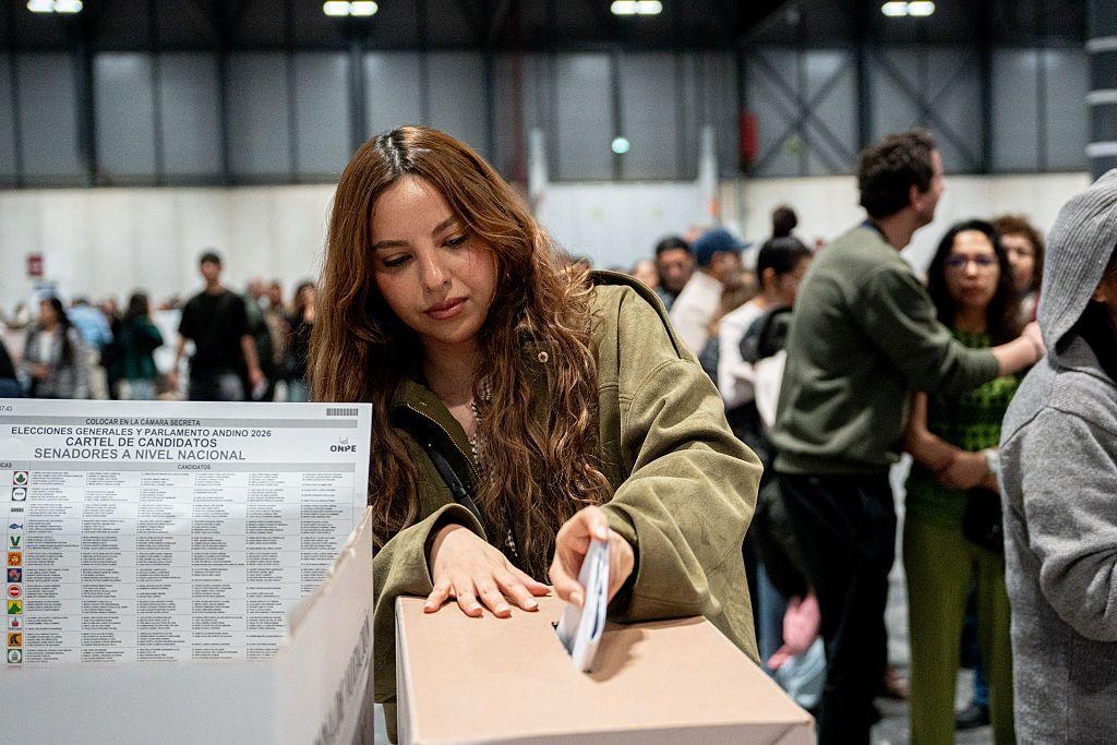 Una mujer deposita su voto en una urna en Madrid, España. Hay otras personas a su alrededor. 