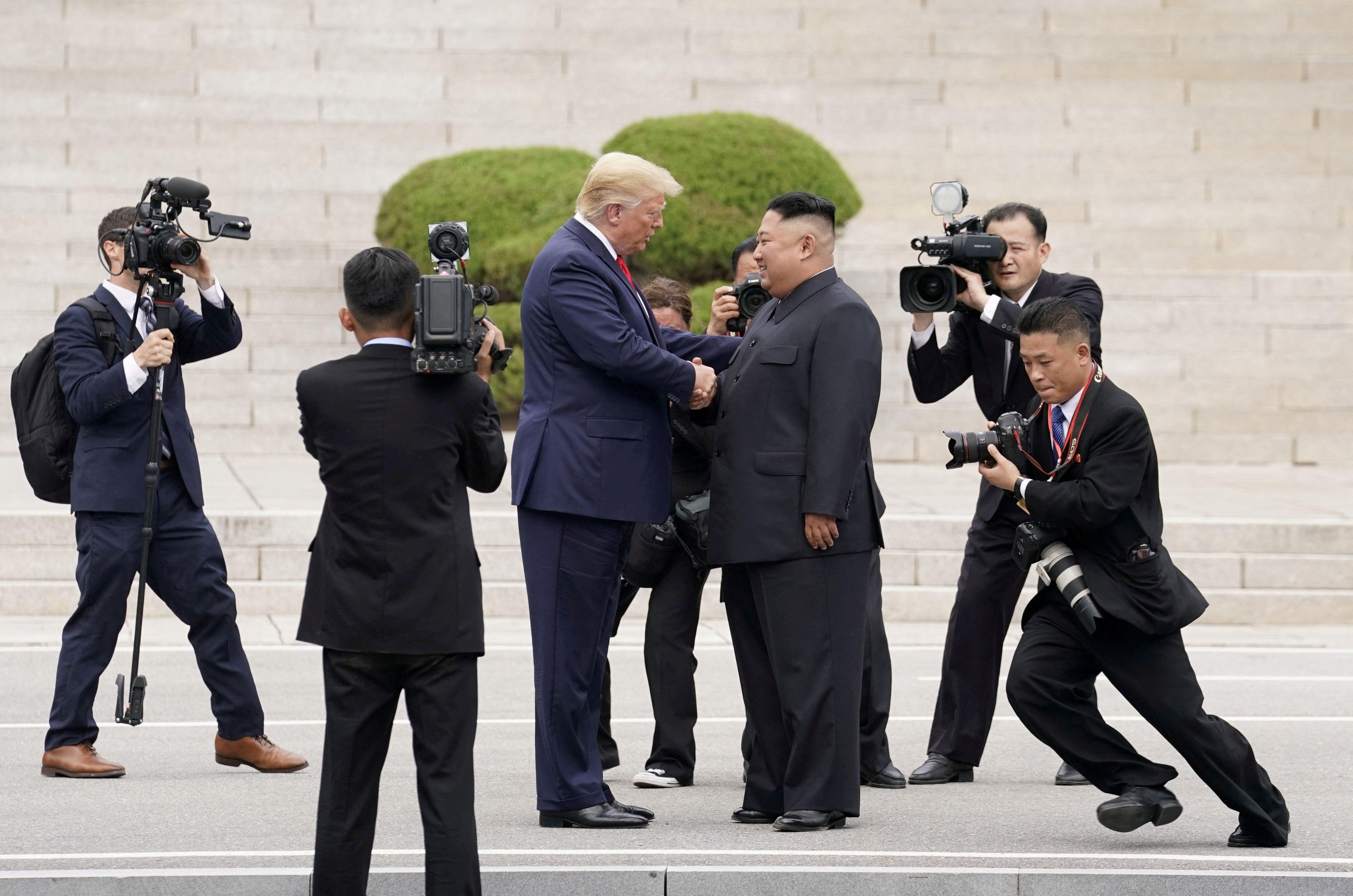 도널드 트럼프 미국 대통령과 김정은 북한 국무위원장이 판문점에서 악수하고 있다. 주변에는 양국 취재진이 두 정상의 만남을 촬영하고 있다.