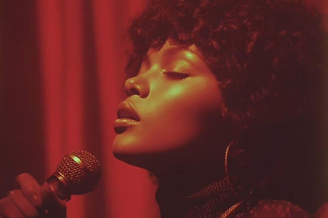 Sienna Rose em outra imagem, com os olhos fechados e microfone à frente, cabelos escuros, grandes brincos e rosto de perfil