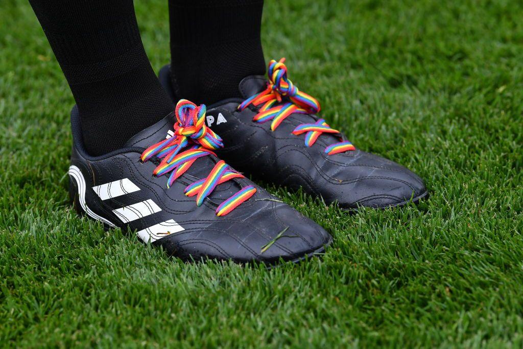 Detalla de los cordones con la bandera LGTBIQ+ en las botas de un árbitro durante un partido de fútbol.