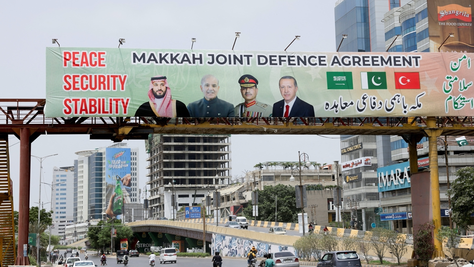 Outdoor em uma passarela de pedestres sobre uma rua mostra os l&iacute;deres da Turquia, Ar&aacute;bia Saudita e Paquist&atilde;o ap&oacute;s a assinatura do Acordo de Defesa Conjunta de Meca, em Karachi, no Paquist&atilde;o, com carros e pessoas passando embaixo