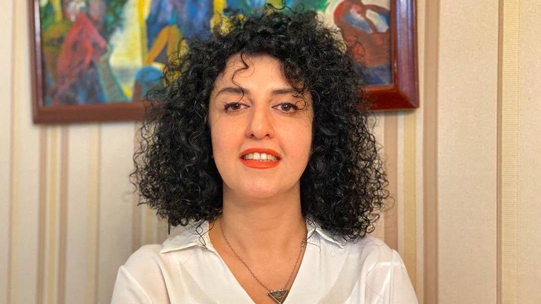 Narges Mohammadi sonríe en esta foto de folleto sin fecha. Tiene el pelo negro rizado y lleva una camisa blanca, un collar en forma de triángulo y lápiz labial rojo.