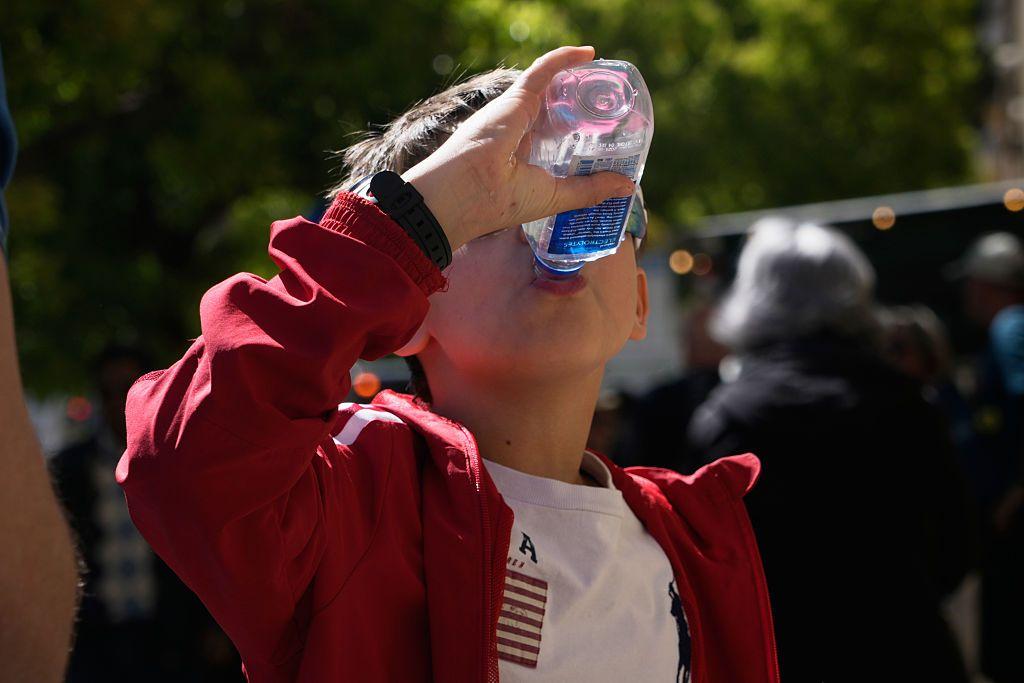 Un niño bebe agua de una botella plástica.
