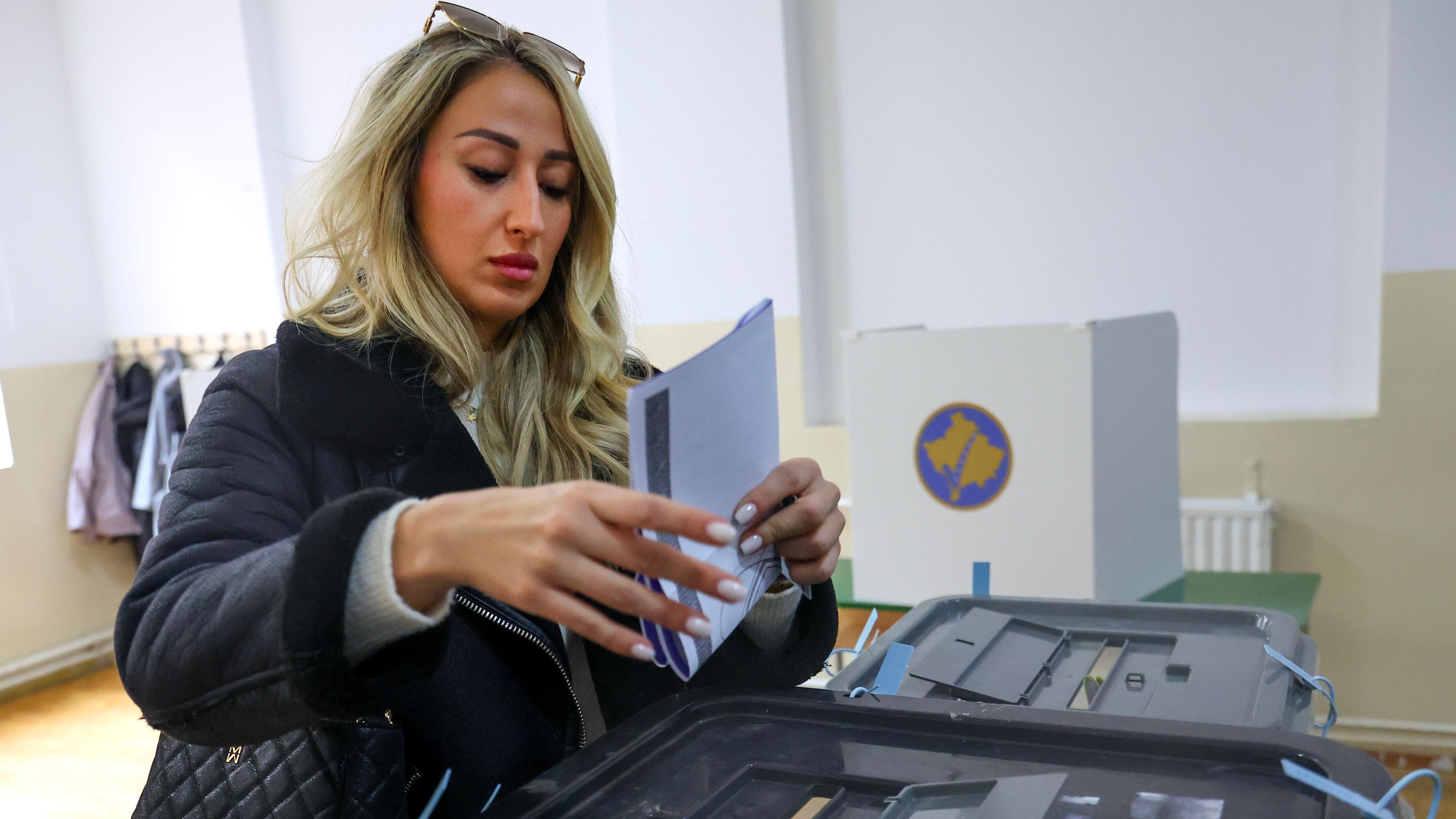 Plavokosa žena spušta glasački listić u kutiju, Severna Mitrovica 12. oktobar 2025.