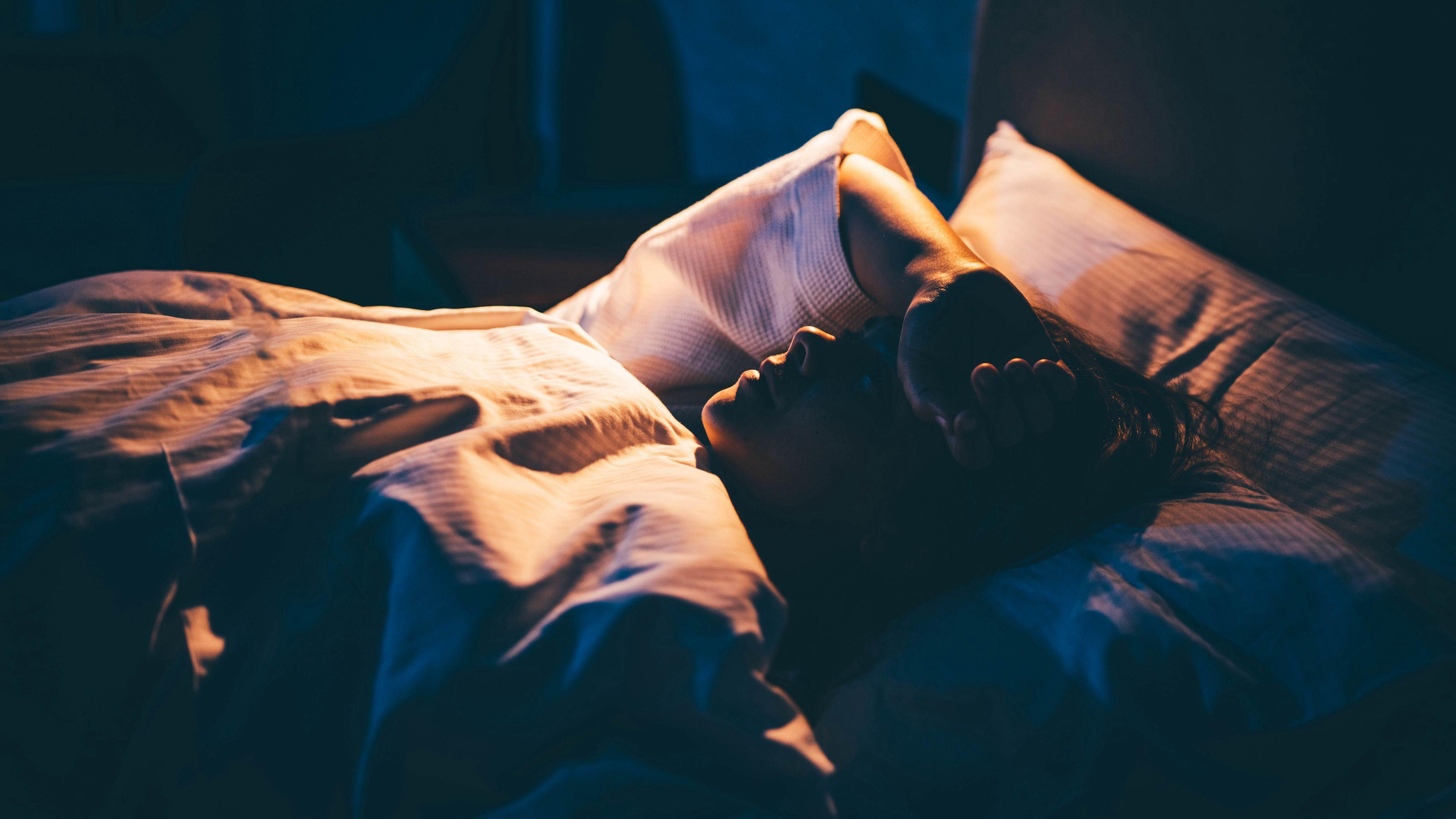 A woman lying awake in bed with her arm across her face.