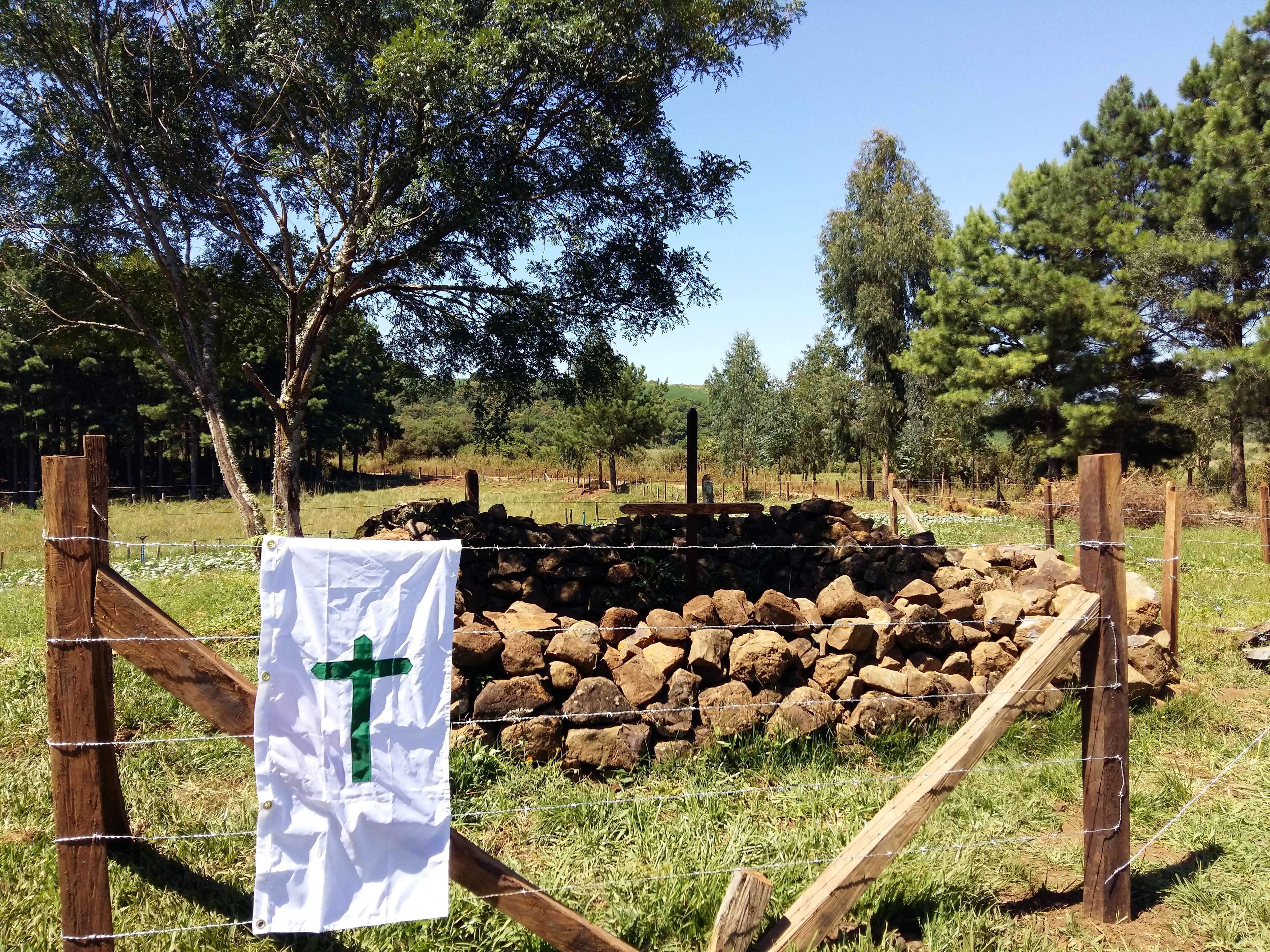 Imagem de um pano branco com desenho de uma cruz pendurado em uma cerca no campo