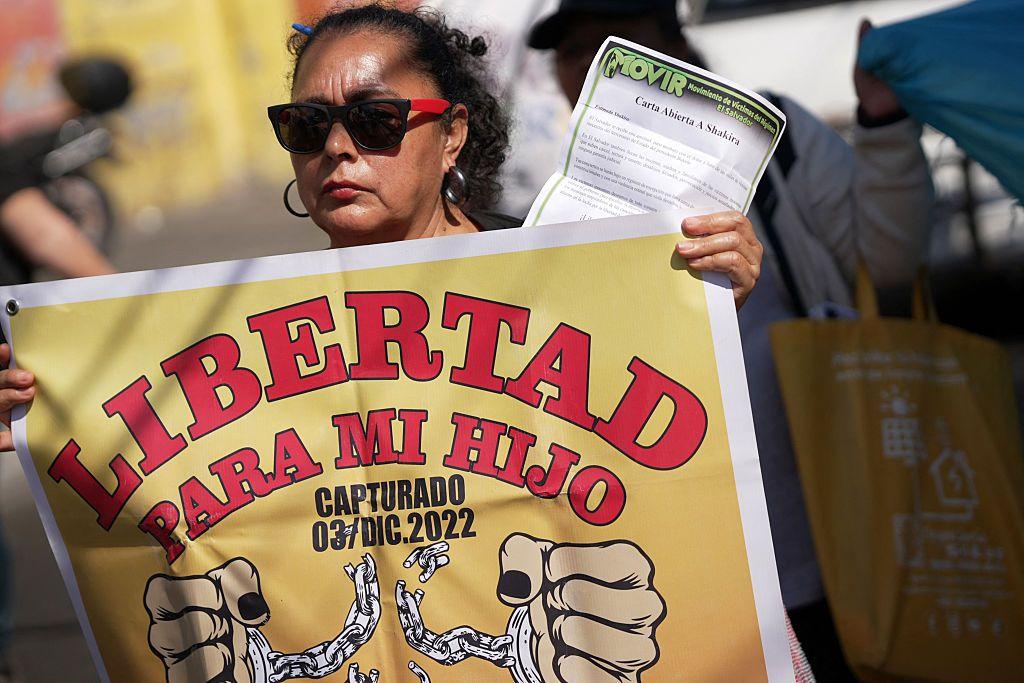 Una mujer con lentes de sol porta una pancarta que dice "Libertad para mi hijo capturado 03/Dic.2022".