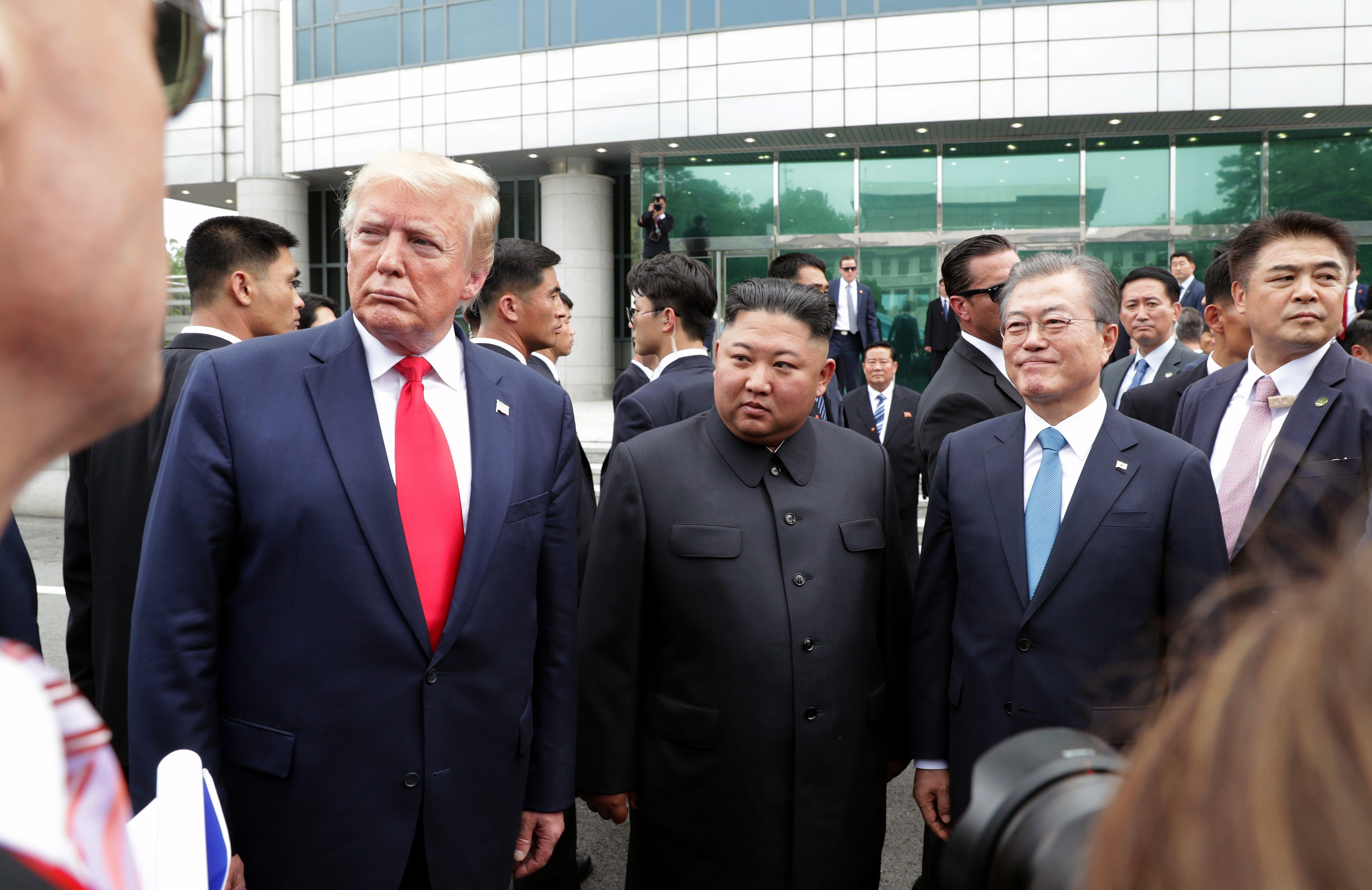 트럼프 대통령, 김정은 위원장, 문재인 전 대통령이 판문점 남측 사무소를 배경으로 포즈를 취하고 있다