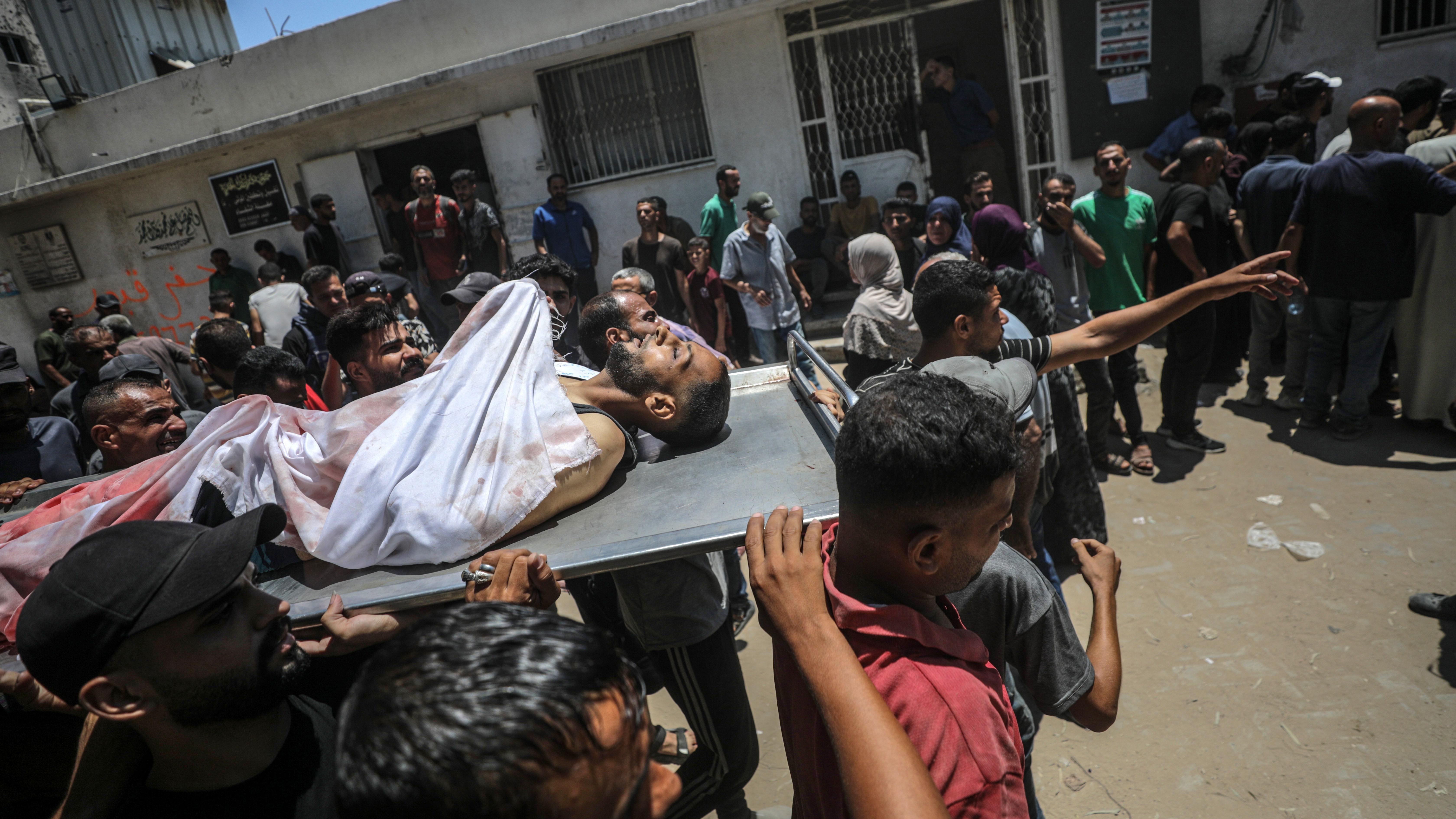  فلسطينيون يحملون جثة رجل بعد أن قُتل بالرصاص في نقطة توزيع طعام بمستشفى الشفاء في مدينة غزة، 20 يوليو/تموز 2025. 