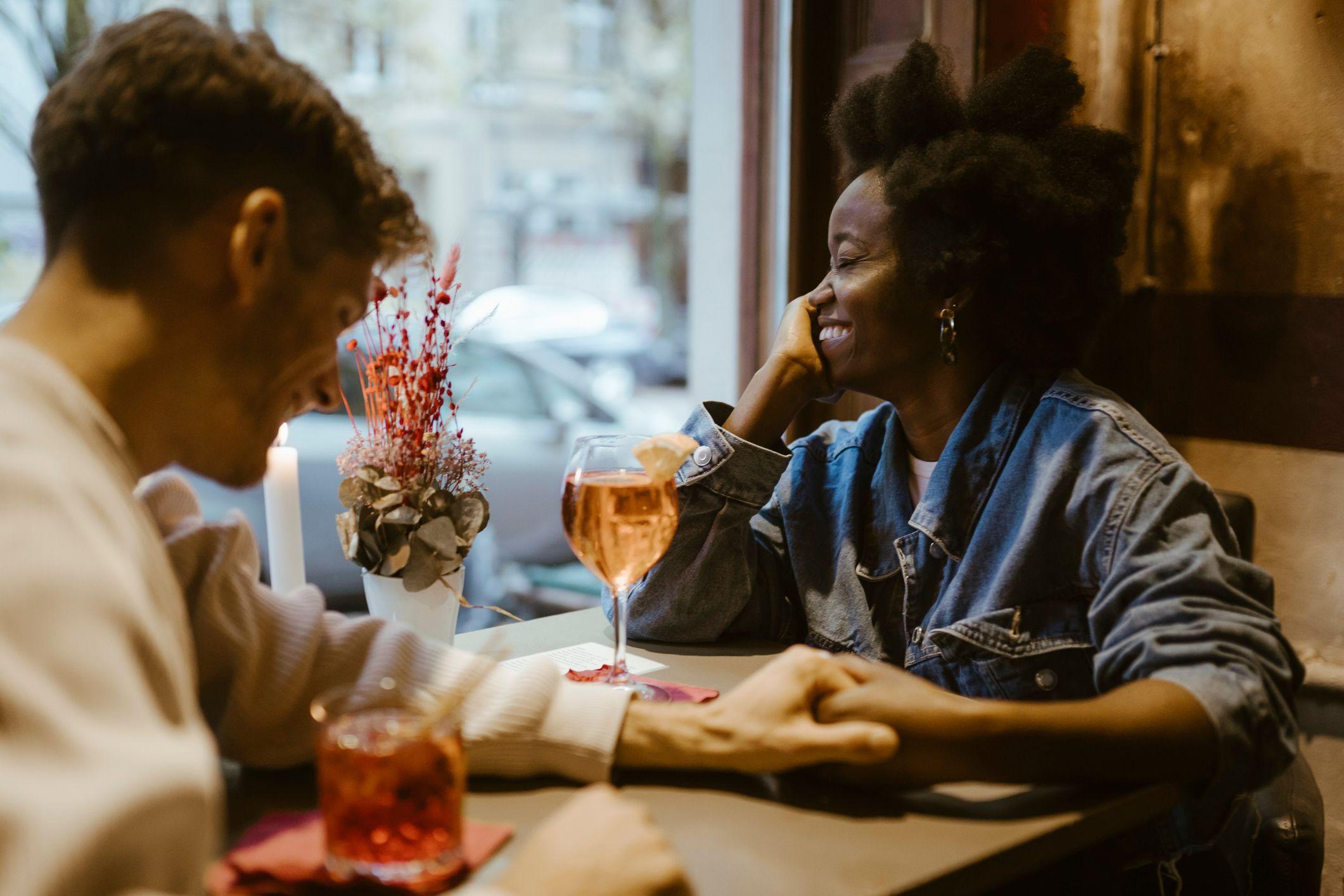Una pareja sentados en una mesa de un restaurant riéndose mientras se agarran de la mano.