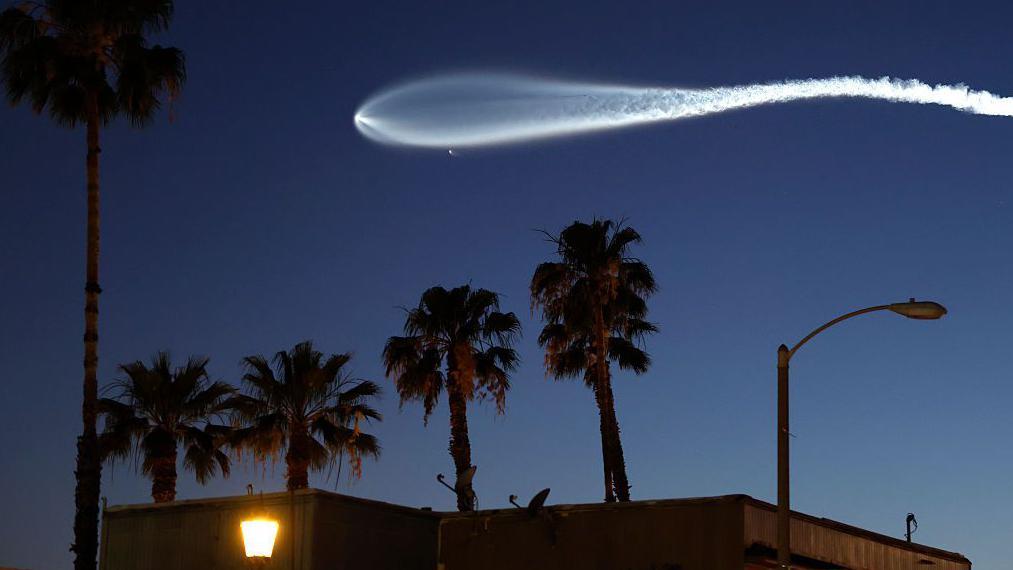 Una estela blanca dejada en el cielo oscuro por un cohete que lleva uno de los satélitles de Starlink.
