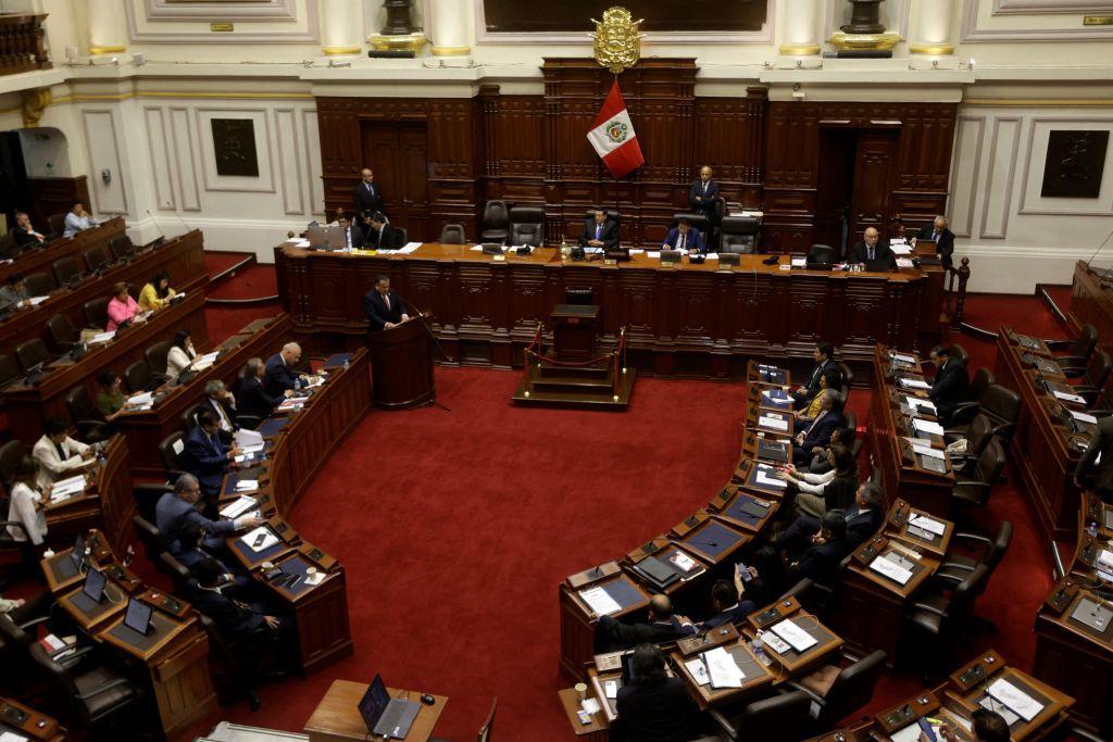 Congresistas sesionan dentro de la cámara del Legislativo, con una bandera de Perú de fondo. 