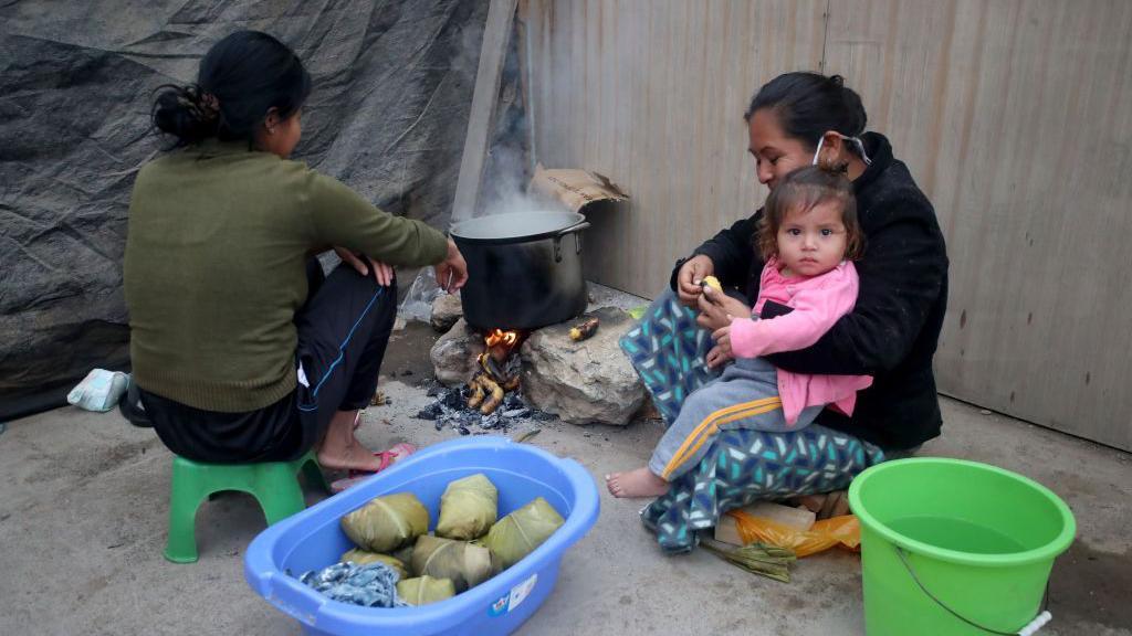 Dos mujeres con una niña en brazos cocinan papas en un barrio humilde de Lima.