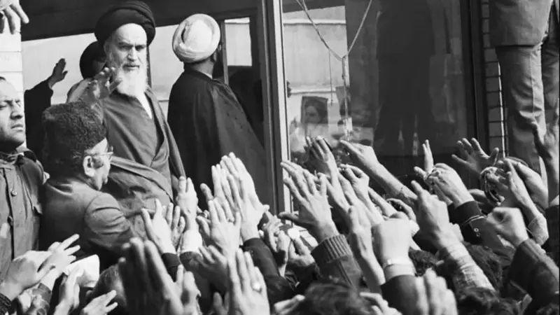 Khomeini rodeado por multidão que ergue os braços em sua direção.