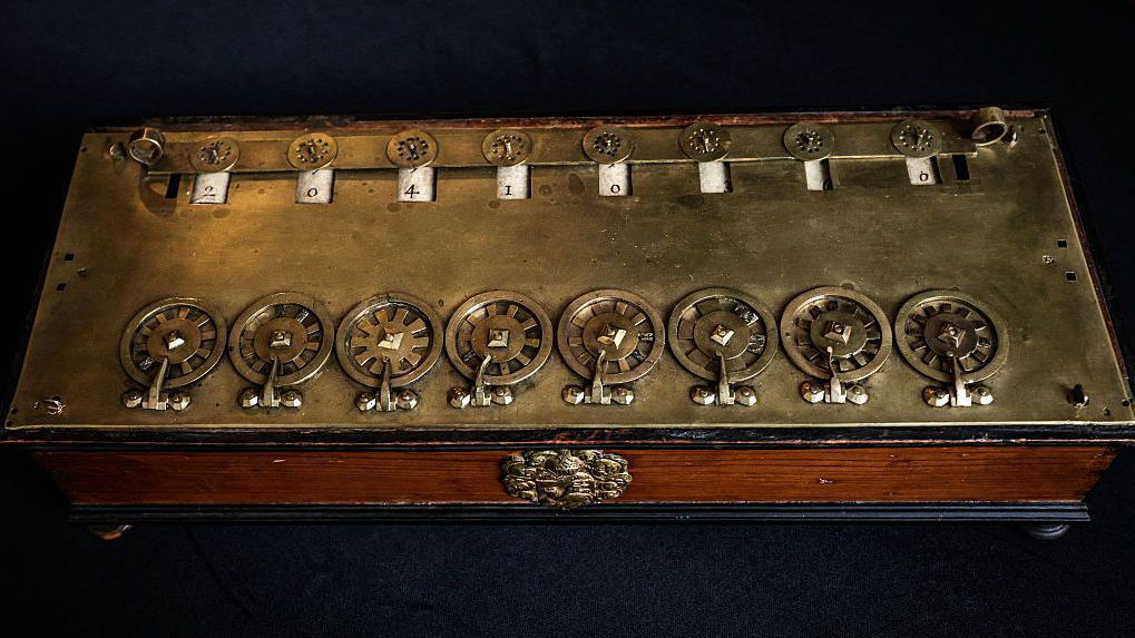 Máquina hecha de madera y bronce con ruedas y números.