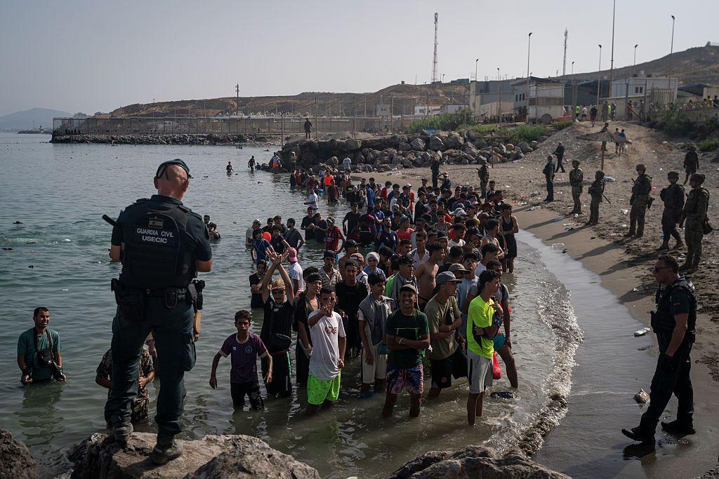 حرس إسبانيون أمامهم مجموعة من المهاجرين من المغرب عبر البحر. الموج هادئ والصورة التقطت نهاراً