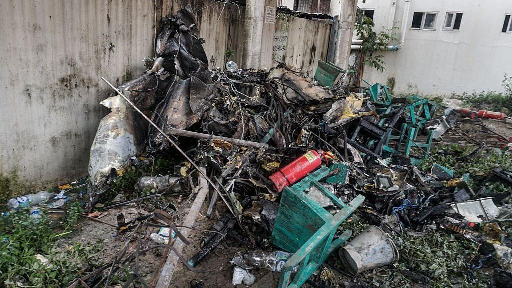 Algunos de los escombros del avión mezclados con sillas de madera de la escuela chamuscadas y un extintor tirados en el suelo