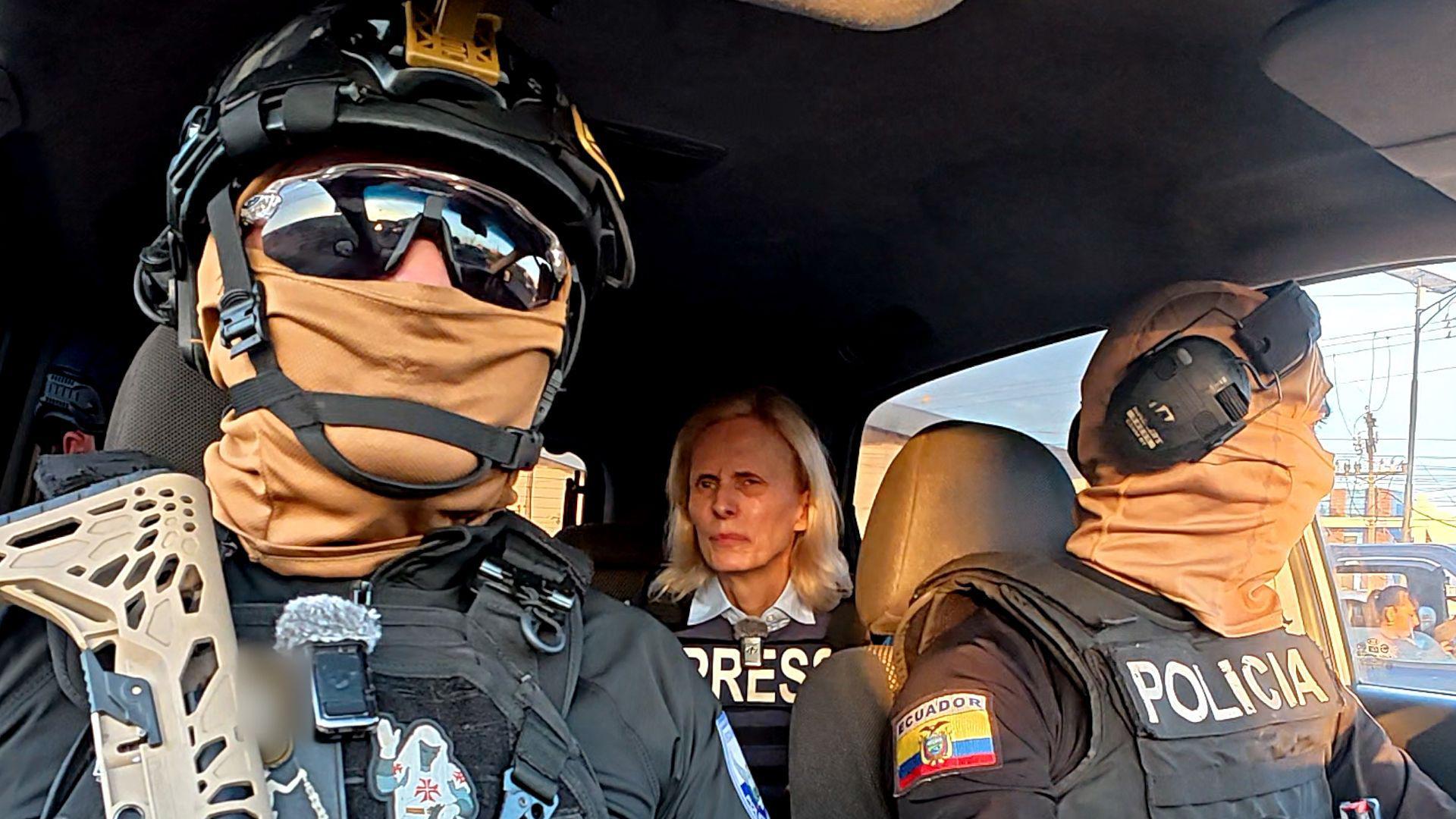 Dos policías ecuatorianos con gafas de sol oscuras, cascos y pasamontañas —que les cubren completamente el rostro— están sentados en un coche frente a Orla Guerin, de la BBC, quien lleva un chaleco antibalas con la palabra "PRENSA" impresa. 