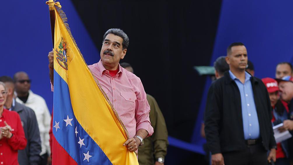 Nicolás Maduro echa un vistazo hacia arriba mientras sujeta una bandera de Venezuela. 