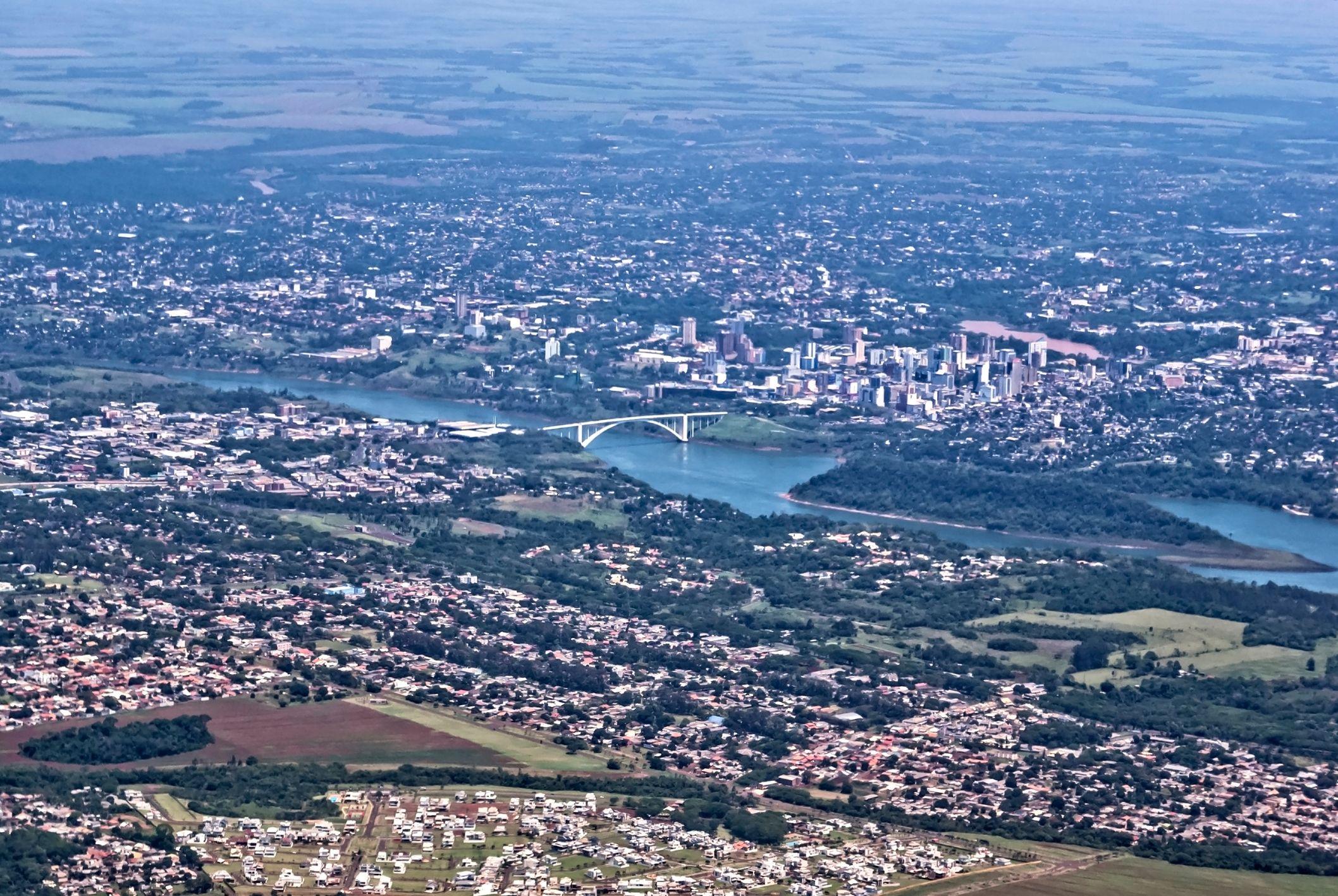 Foto aérea da região fronteiriça; é possível ver Rio Paraná e ponte
