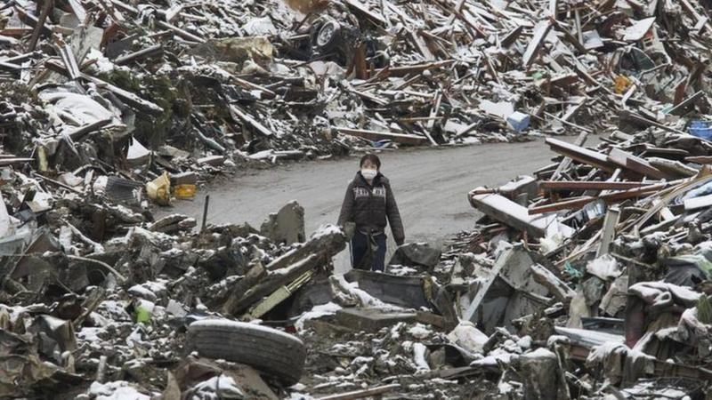 Uma mulher caminha entre os escombros na cidade japonesa de Minamisanriku, no norte do Japão, após o tsunami de 2011.