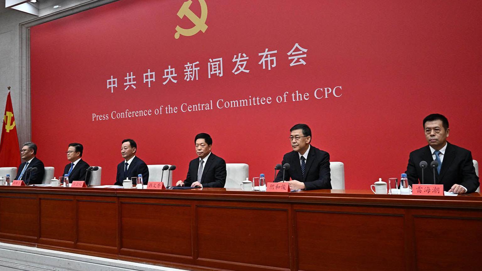 中共成員圍坐在紅色背景前的桌子旁。