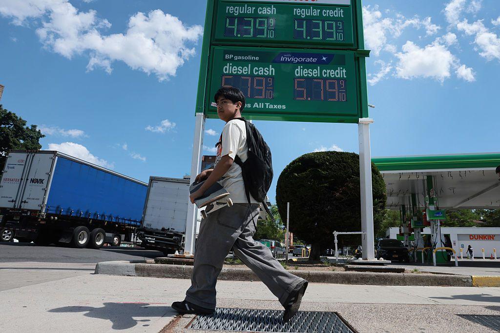 Un hombre pasa frente a una gasolinera, donde se muestran los precios por galón, en Nueva York