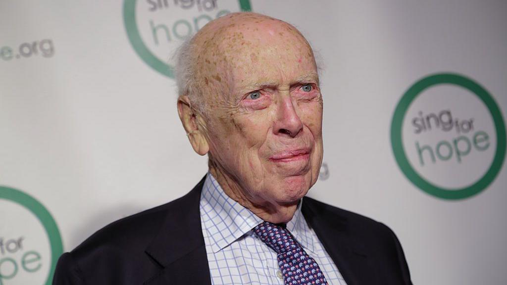 Imagen de James Watson tomada en 2016, cuando tenía 89 años. Viste una chaqueta oscura, una camisa blanca con rayas finas y una corbata violeta con detalles celestes y rosados.