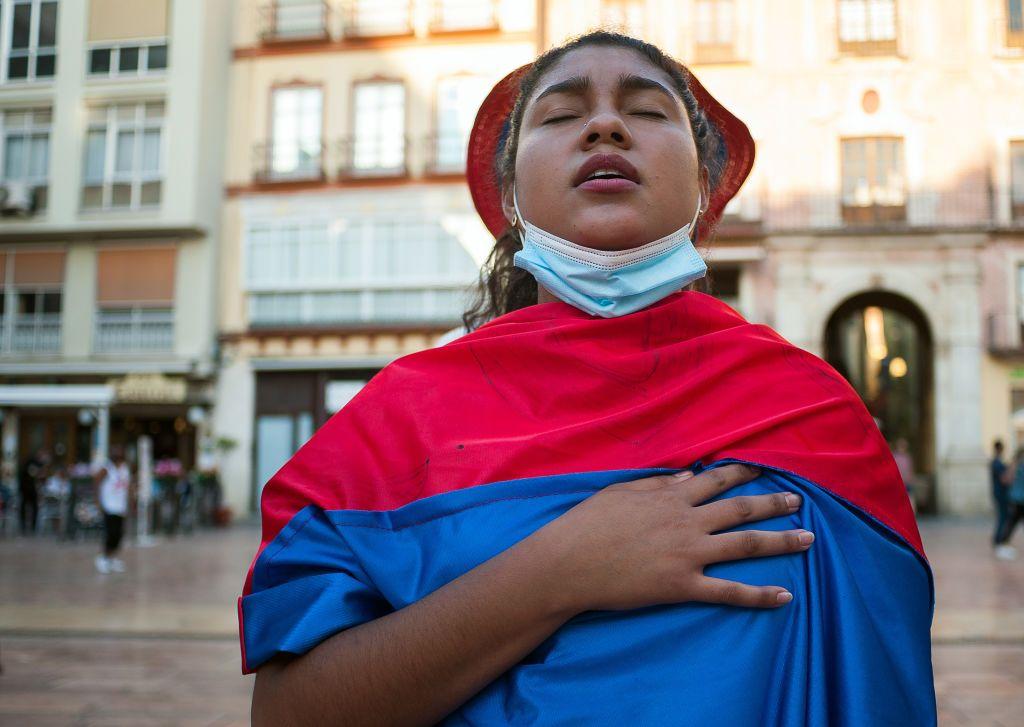 Mujer con la bandera de colombia en medio de una plaza española. 