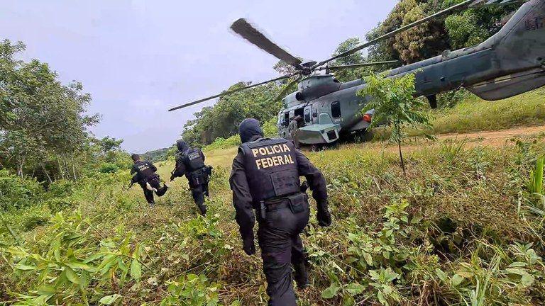 Foto mostra agentes da PF se aproximando de um helic&oacute;ptero em uma &aacute;rea de floresta na Terra Ind&iacute;gena Yanomami, em Roraima