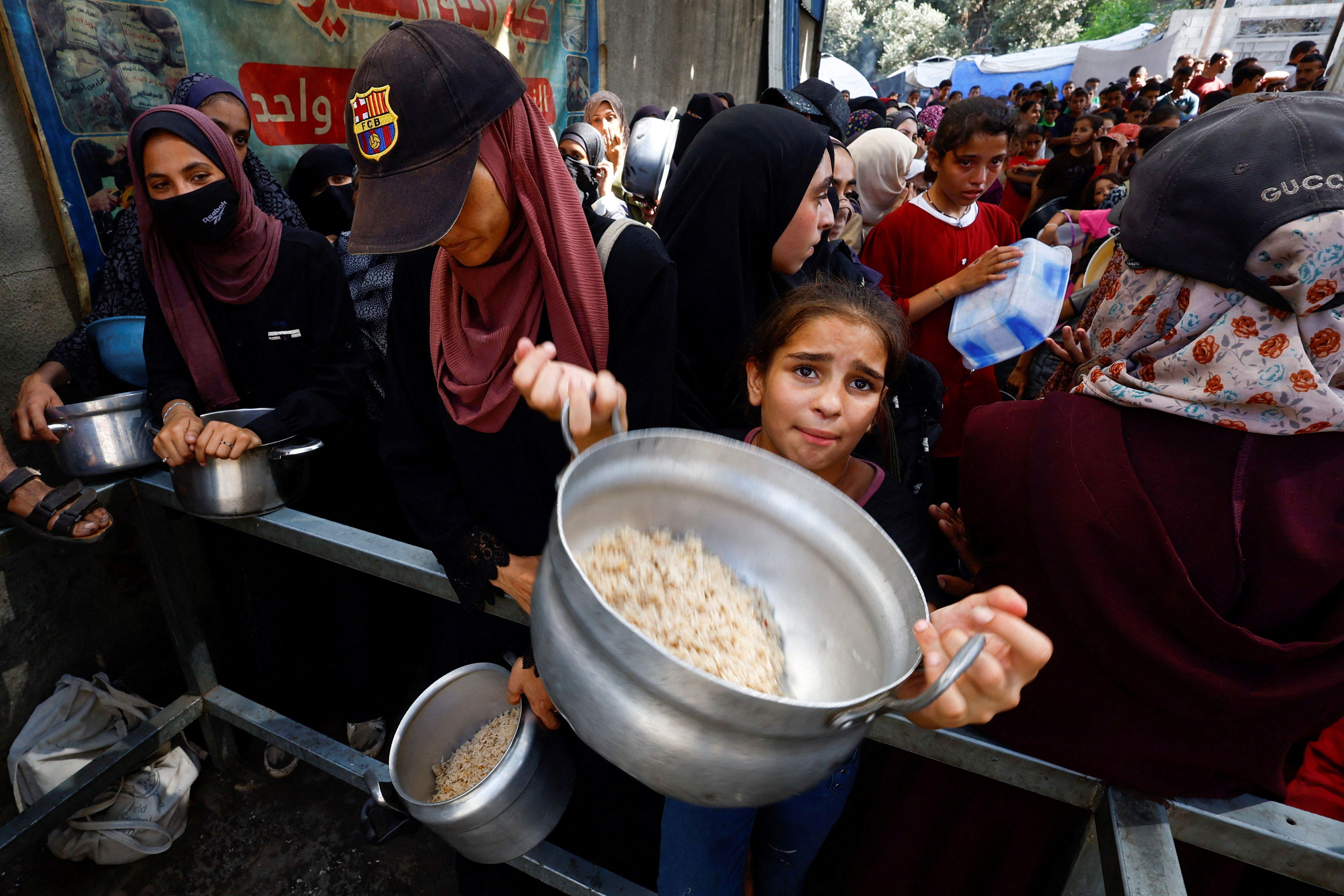 طفلة تحمل وعاءً وتنظر إلى الكاميرا وسط الزحام، تطلب طعاماً من مطبخ خيري في النصيرات وسط قطاع غزة، 28 سبتمبر 2025