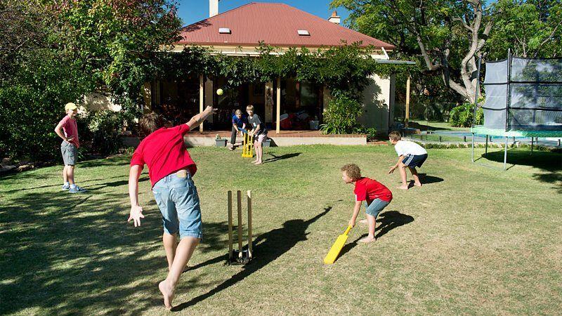 Fam&iacute;lia jogando cr&iacute;quete em dia de sol, no quintal de casa