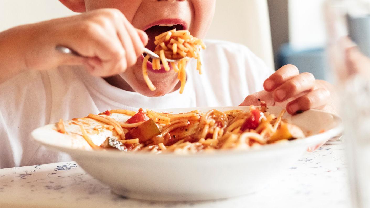 Niño comiendo spaghetti con salsa de tomate en una cocina.