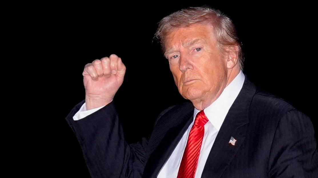 Donald Trump con una corbata roja y levantando el puño.