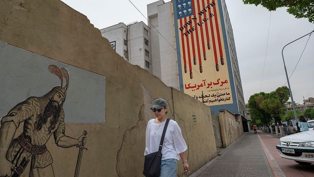 Una joven iraní camina por una acera bajo un mural antiestadounidense en el centro de Teherán, Irán.

