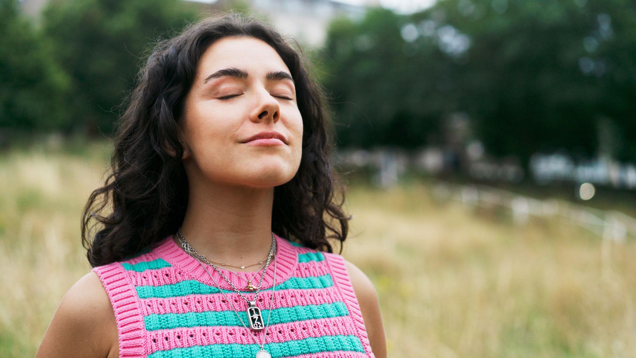 Una mujer jover respira en un lugar verde y abierto. 