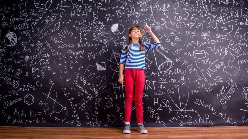 فتاة صغيرة تقف أمام لوح كتبت عليه بالطبشور معادلات رياضية 