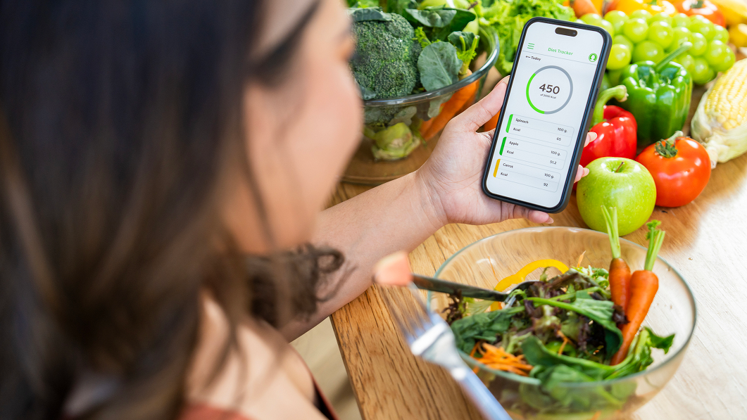 Pessoa comendo salada olhando para um contador de calorias no celular