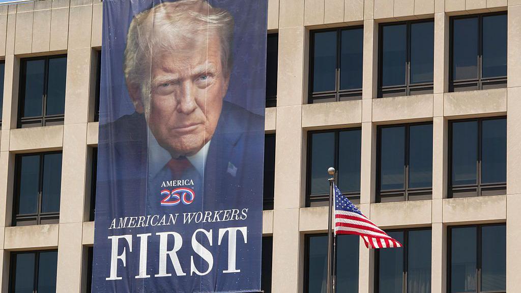 En el exterior del Edificio Frances Perkins del Departamento de Trabajo se lee en una pancarta con el retrato de Trump, 