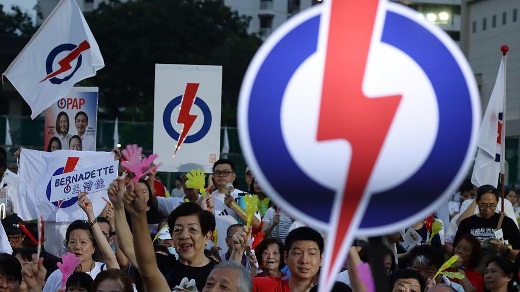 新加坡人民行動黨支持者在選舉集會上歡呼，許多人高舉海報和旗幟，上面印有該黨的標誌：藍白相間的圓圈中有一個紅色閃電