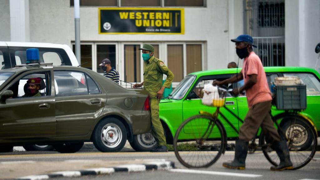 Carros e pessoas paradas em uma rua, em frente &agrave; sucursal da Western Union em Havana