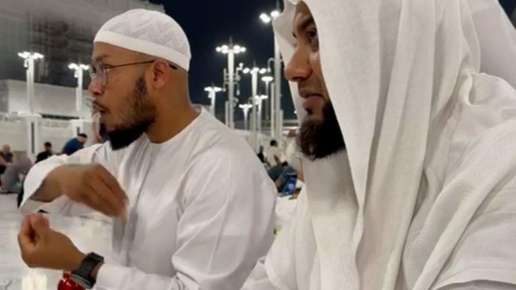 رجلان يرتديان ملابس إسلامية بيضاء يجلسان في فضاء معماري واسع ومضيء، تتخلله أعمدة عالية وأضواء في الخلفية، ويتواصلان باستخدام لغة الإشارة. ويستخدم أحدهما، الجالس على اليسار، لغة الإشارة البريطانية.