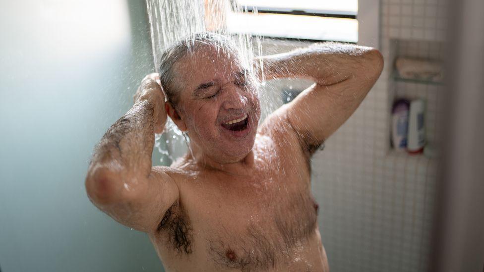 Homem tomando banho alegremente no chuveiro, de dia