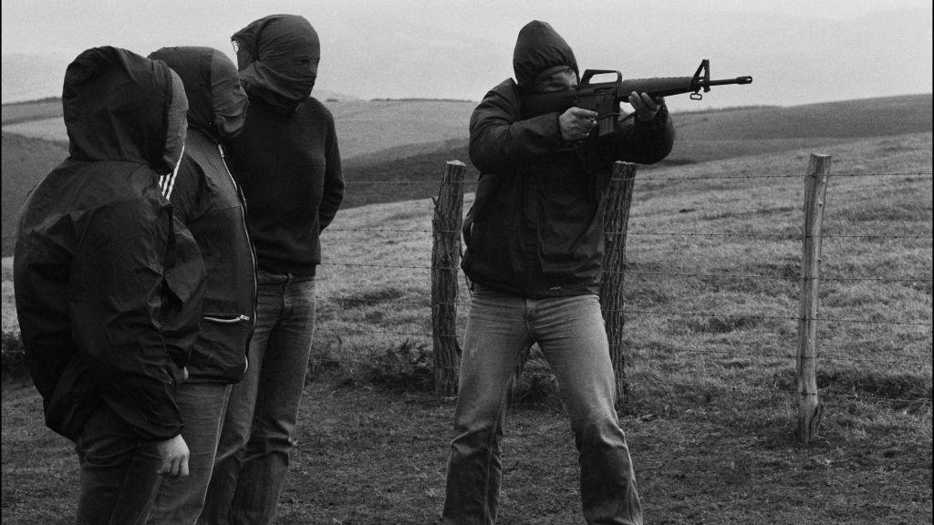 Membro encapuzado do ETA aponta um fuzil durante treinamento. Outros três militantes, também encapuzados, o observam em imagem de 1978.