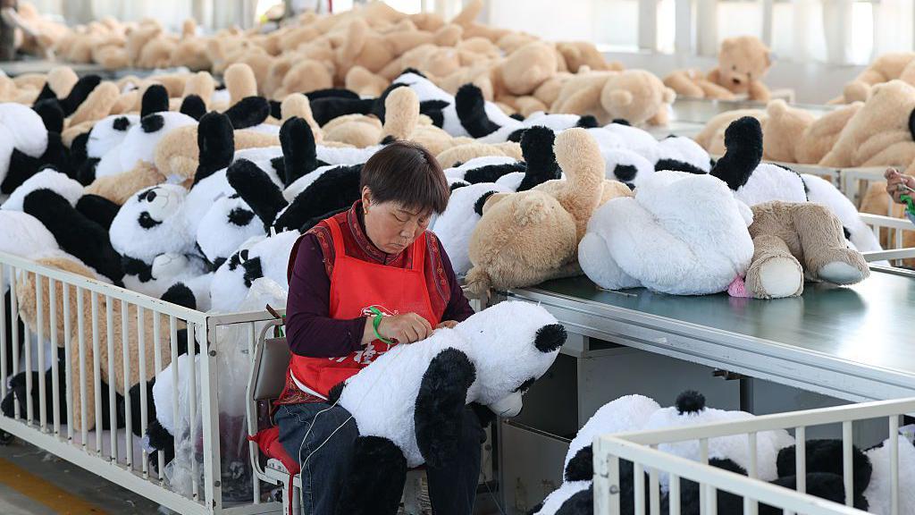Uma mulher em uma f&aacute;brica costura pandas de brinquedo fofinhos