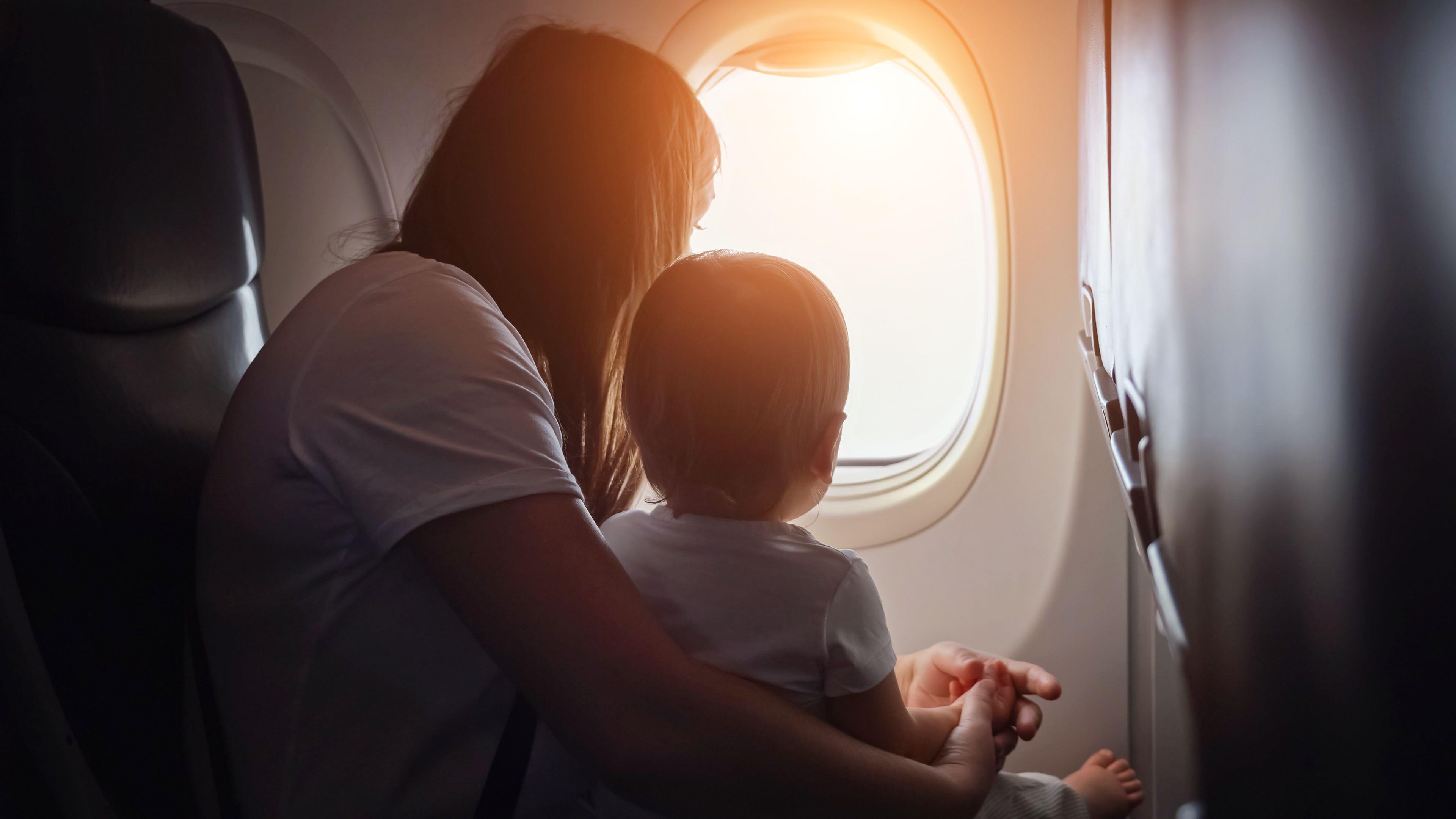 Mulher com criança no colo. Ambos aparecem de costas, olhando pela janela do avião