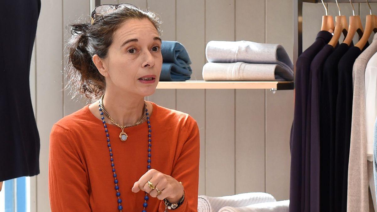Orsola de Castro é uma mulher branca. Ela está usando uma blusa laranja e colares. Ela está com cabelo preso.